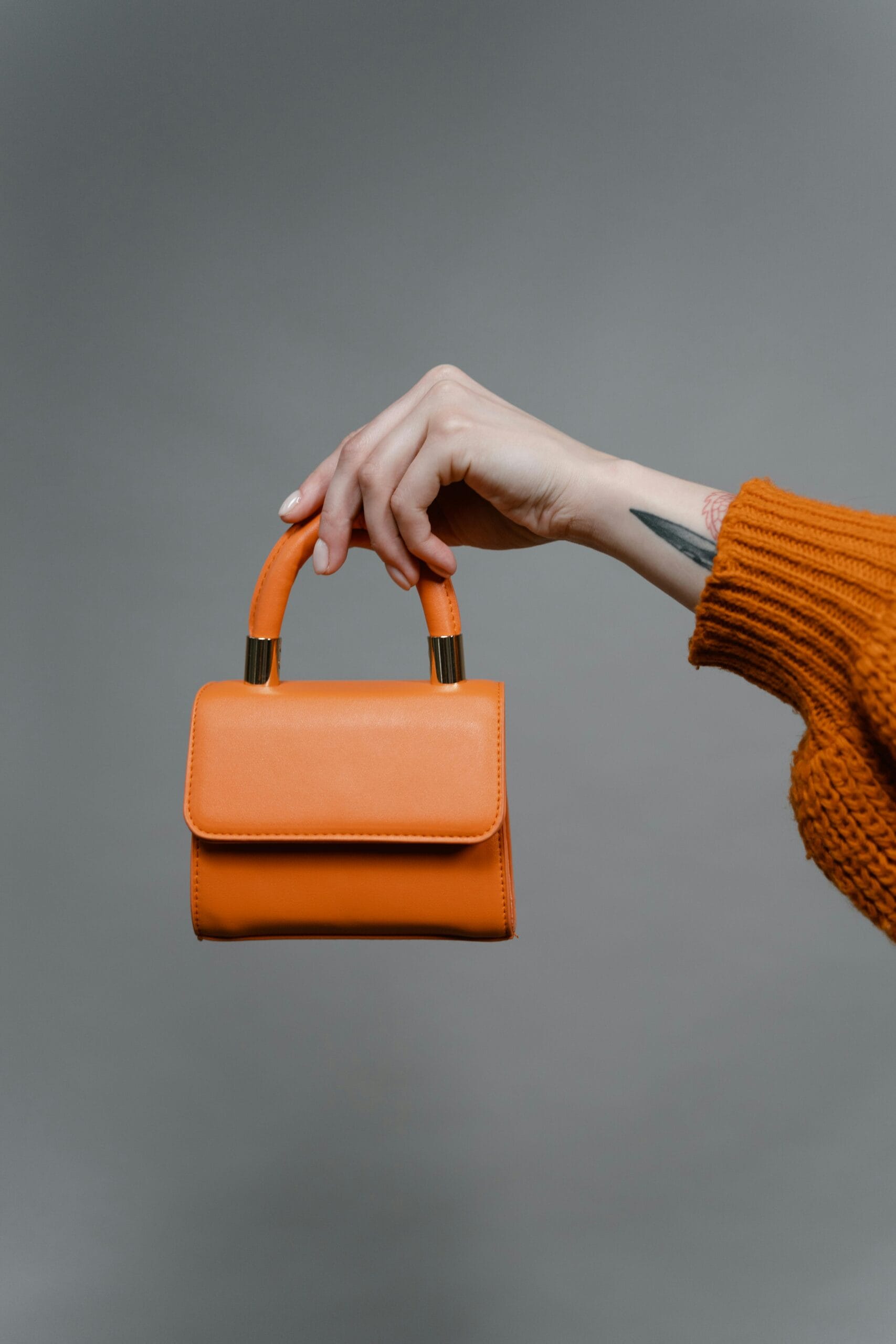Minimalist vibrant orange leather mini handbag held by hand - Jawaher